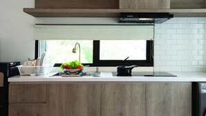 A modern kitchen with a built-in dishwasher, a window with a view, and a wooden cabinet. - Ariama Serviced Residence (Jakarta)