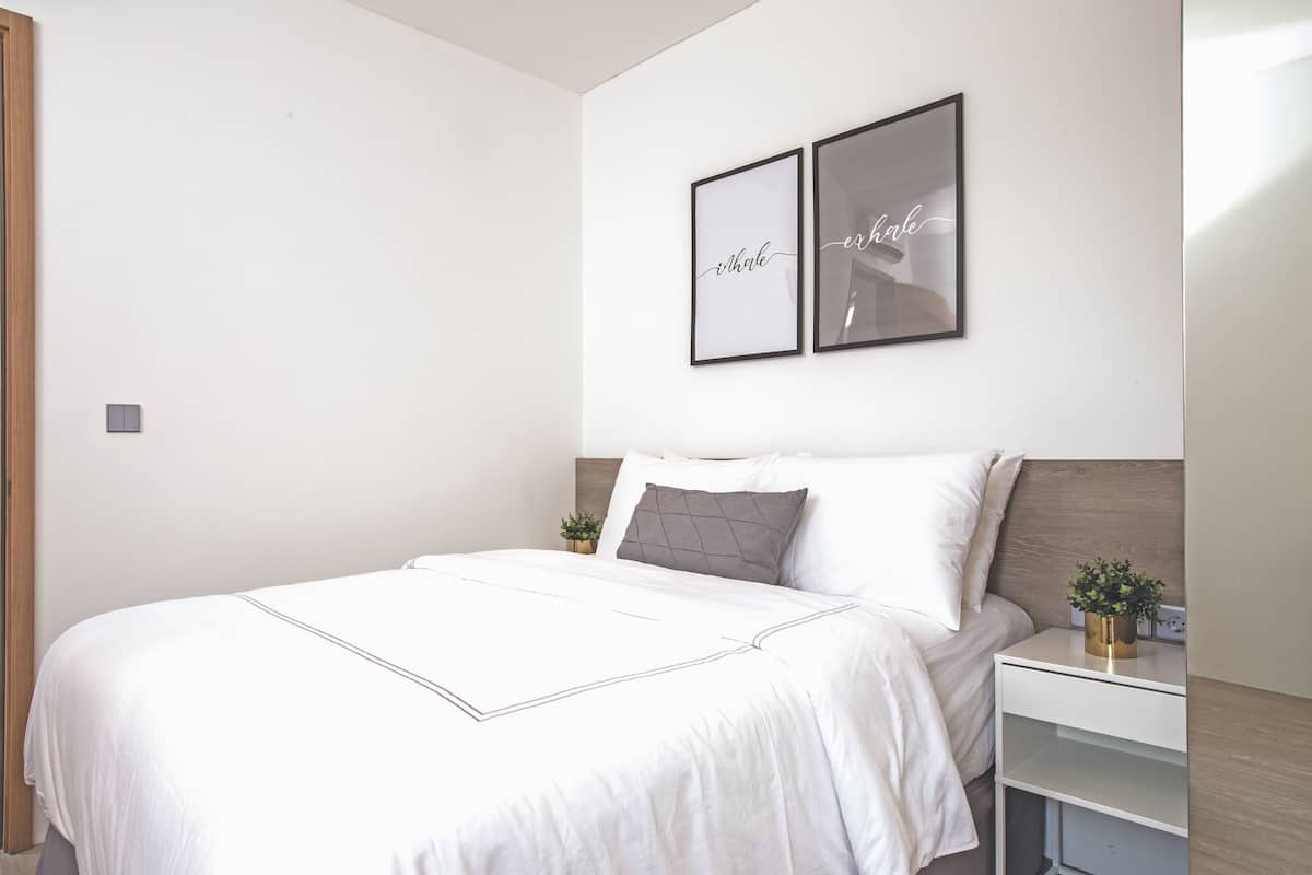 A neatly made bed with a white duvet and two pillows, a bedside table with a plant, and two framed pictures on the wall.