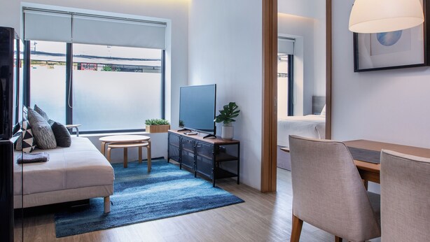 A modern living room with a sofa, TV, dining table, chairs, and a large window. - Ariama Serviced Residence (Jakarta)