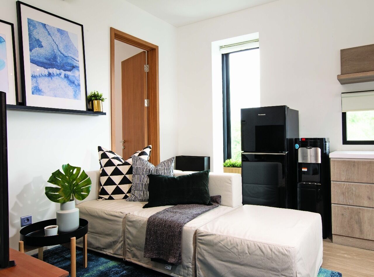 A modern living room with a sofa, a coffee table, a water dispenser, and a refrigerator.