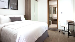 A modern bedroom with a large bed, a desk with a chair, and a wardrobe. - Ariama Serviced Residence (Jakarta)