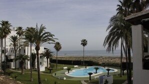 Ein Poolbereich mit Palmen und Liegestühlen, umgeben von Gebäuden mit Blick auf den Strand.