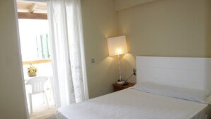 Ein Hotelzimmer mit einem Bett, einem Nachttisch mit Lampe, einem Stuhl vor der Tür und Blick auf einen Balkon mit Tisch und Blumen.