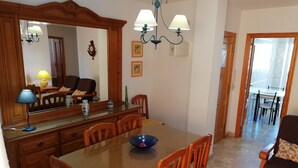 A dining area with a wooden table, chairs, and a chandelier. There is a mirror above the table and a clock on the wall. - Delfines Bl. VII 2º  Solo Familias! (Xeraco Playa)