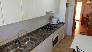 A kitchen with white cabinets, a granite countertop, a stainless steel sink, a microwave, and a stove. - Delfines Bl. VII 2º  Solo Familias! (Xeraco Playa)