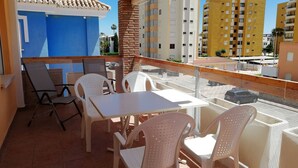 A balcony with white plastic chairs and a table, overlooking a street with buildings. - Delfines Bl. VII 2º  Solo Familias! (Xeraco Playa)