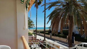 Un balcon avec vue sur la plage, les palmiers et une voiture garée.