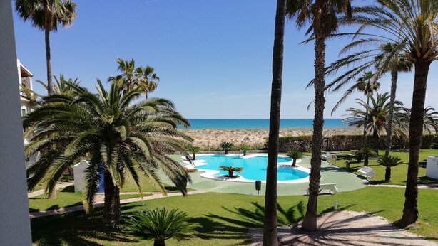 A pool area with palm trees, a view of the beach, and a clear sky. - Deltamar 44 Solo Familias! (Xeraco Playa)