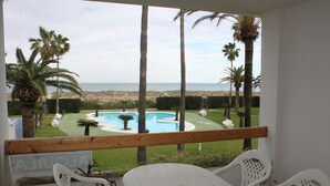 A balcony with a view of a swimming pool, palm trees, and a beach. - Deltamar 44 Solo Familias! (Xeraco Playa)