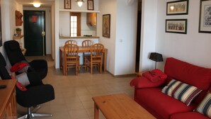A living room with a red sofa, wooden dining table, and chairs. There is a black office chair, a wooden coffee table, and a lamp on a side table. - Deltamar 44 Solo Familias! (Xeraco Playa)