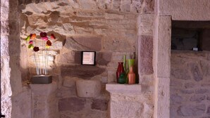 A stone-walled room with a wicker basket, a framed picture, and a shelf with vases. - Gite *** "La Cour pavée" (Sébrazac)