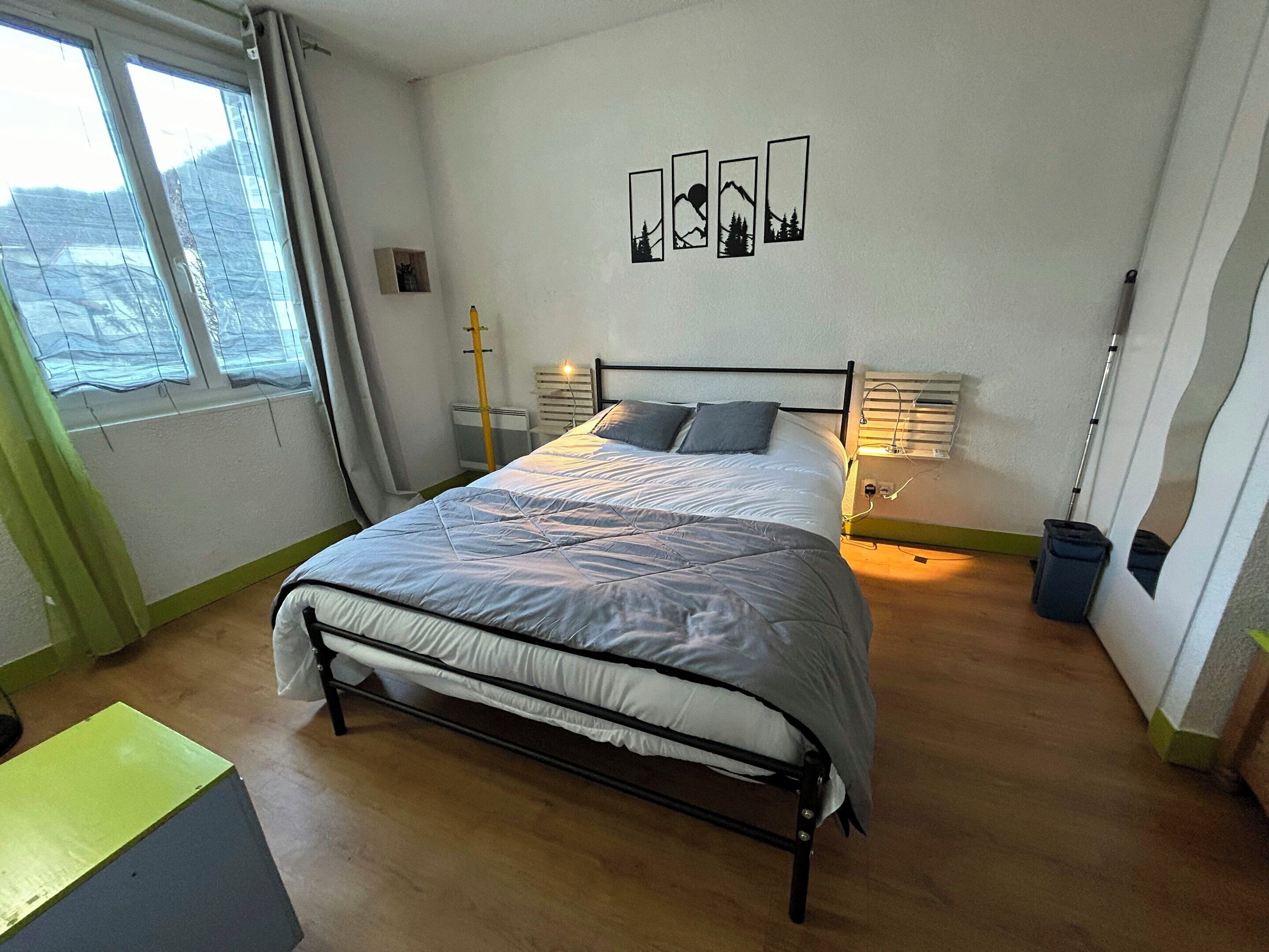 Ein Schlafzimmer mit einem Bett, Nachttischen, einem Fenster mit Vorhängen und Wandbildern.