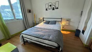 Ein Schlafzimmer mit einem Bett, Nachttischen, einem Fenster mit Vorhängen und Wandbildern.