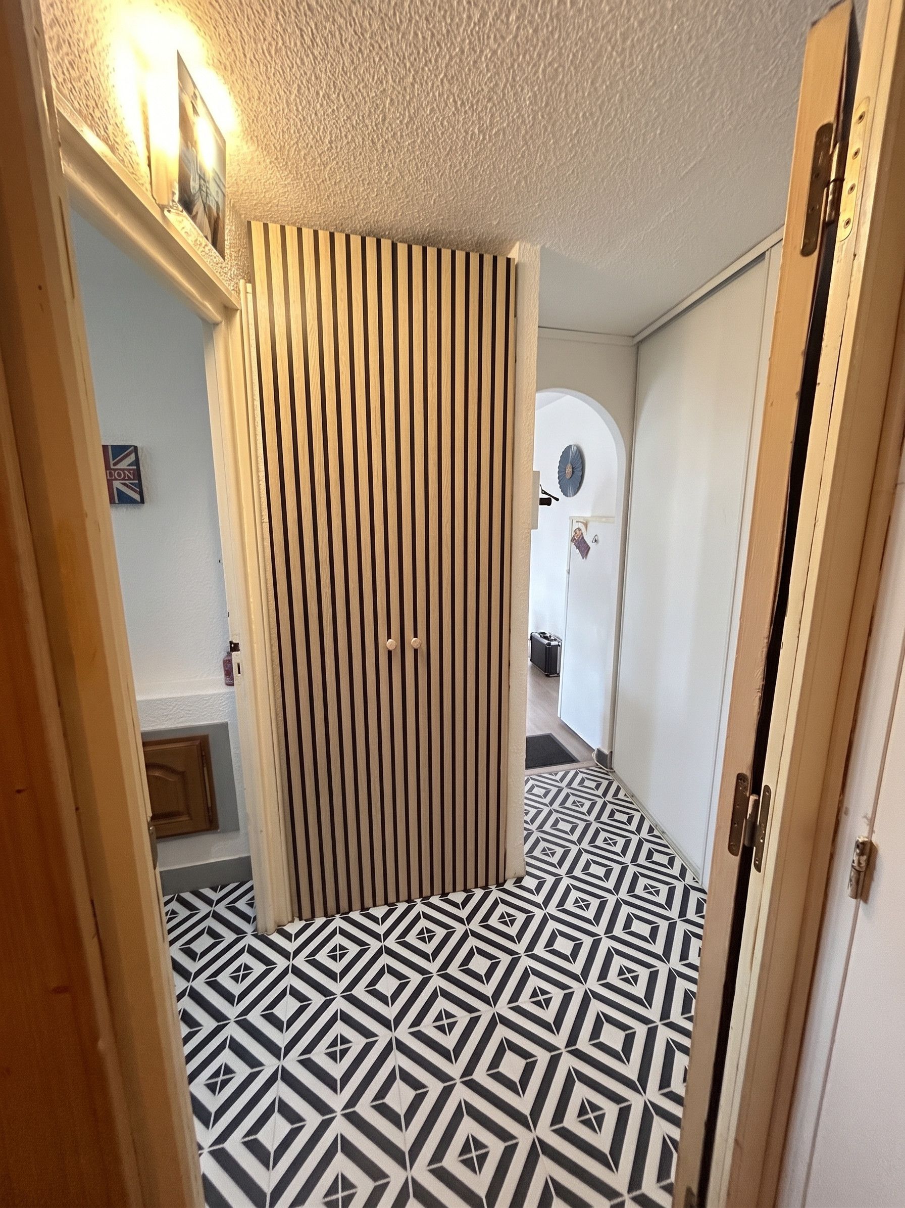 Un couloir étroit avec un sol à motifs, une porte coulissante et une porte donnant sur une autre pièce.