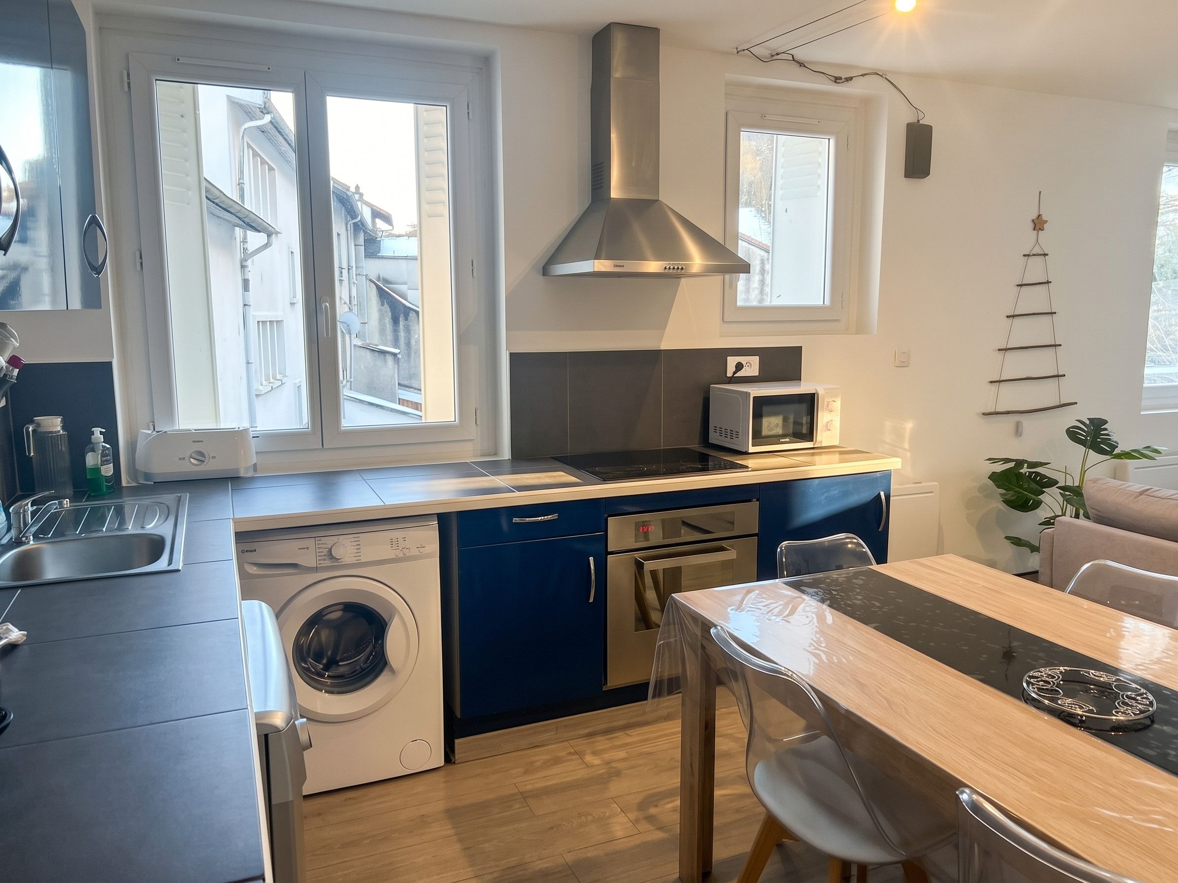 Une cuisine compacte équipée d’un lave-linge, d’un four à micro-ondes et d’un coin repas avec une table et des chaises.