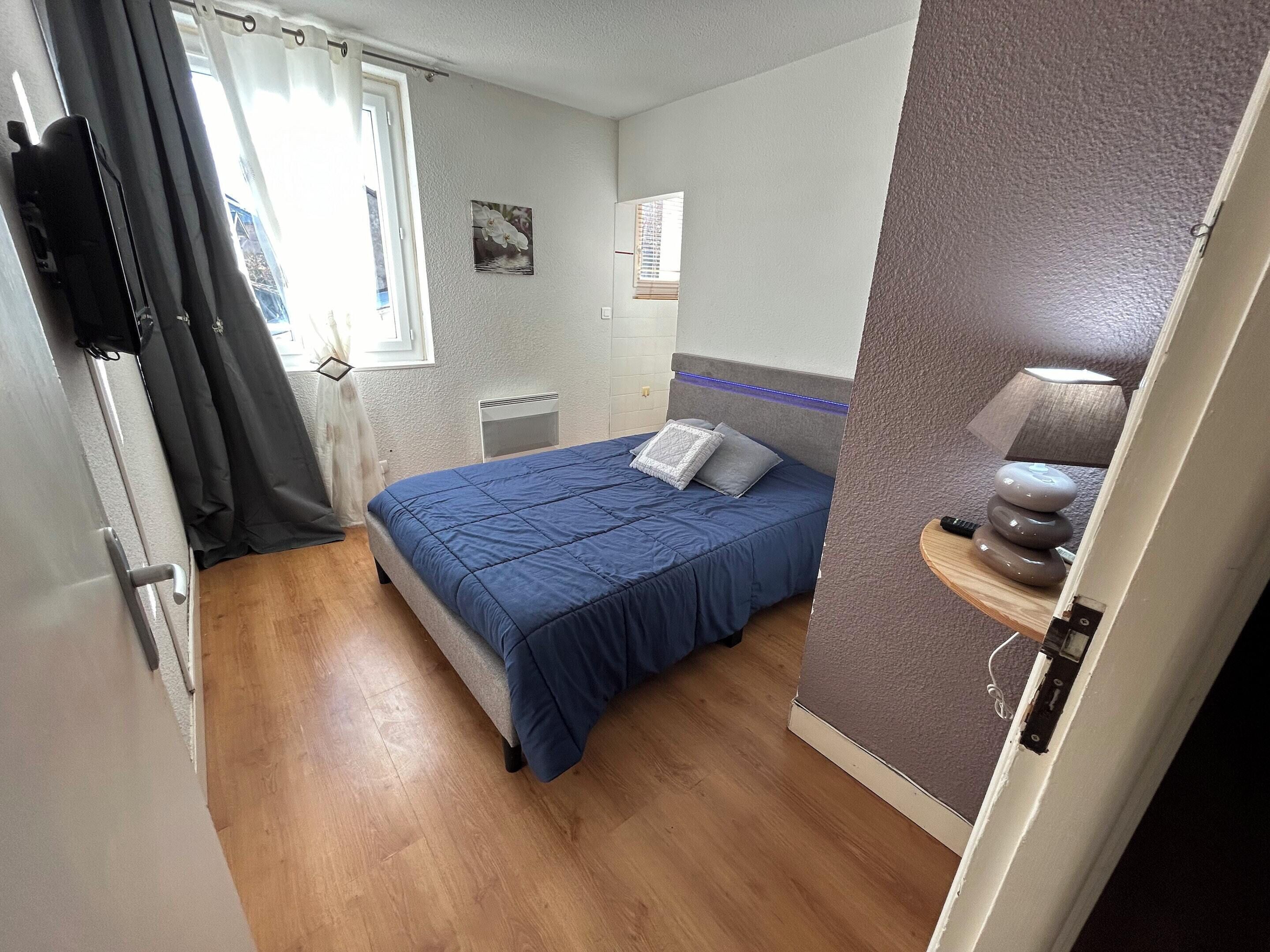 Quarto com cama, mesa de cabeceira com abajur, janela com cortinas e um quadro na parede.