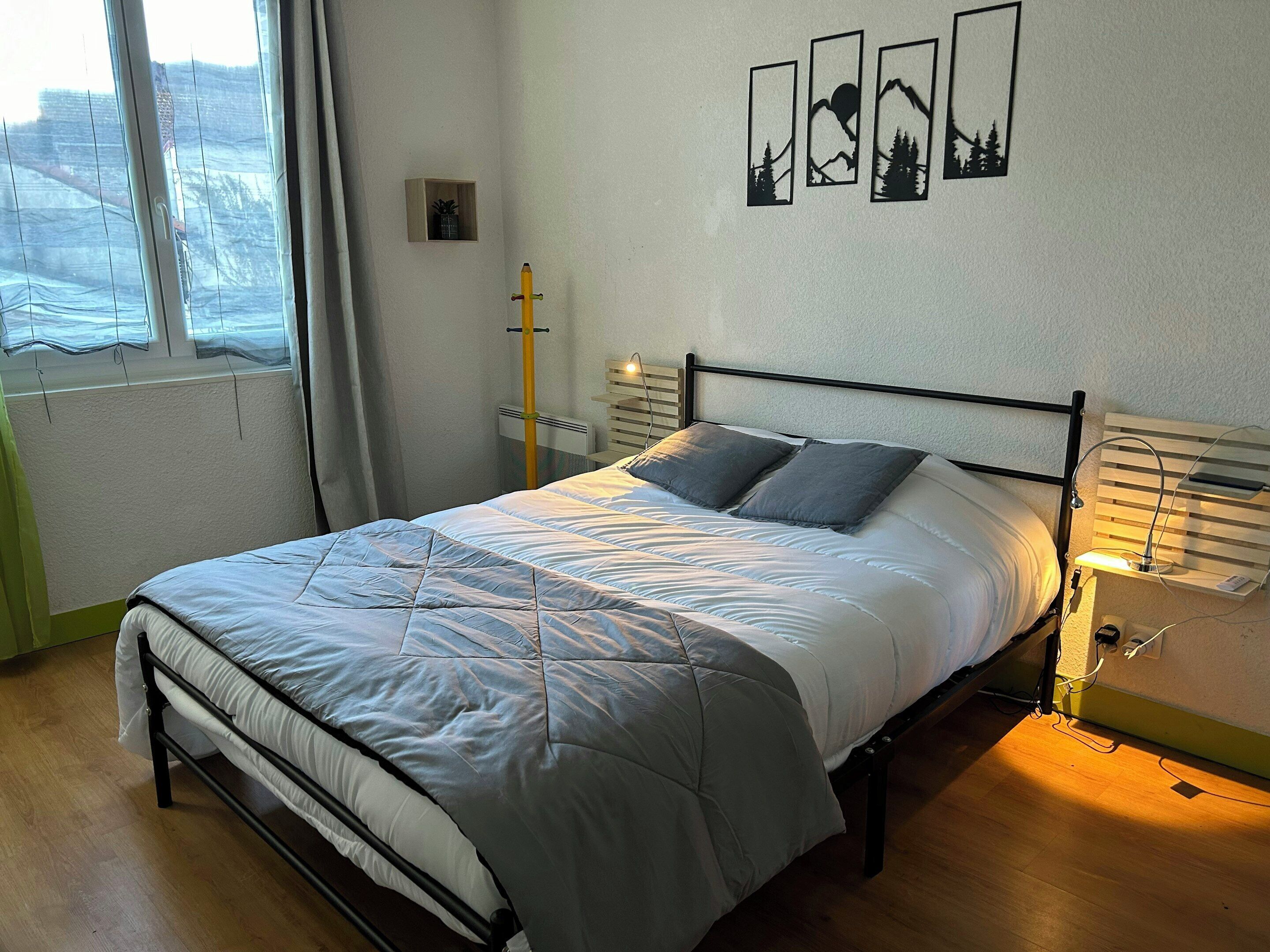 A neatly made bed with a grey and white duvet, a bedside table with a lamp, and a window with curtains.