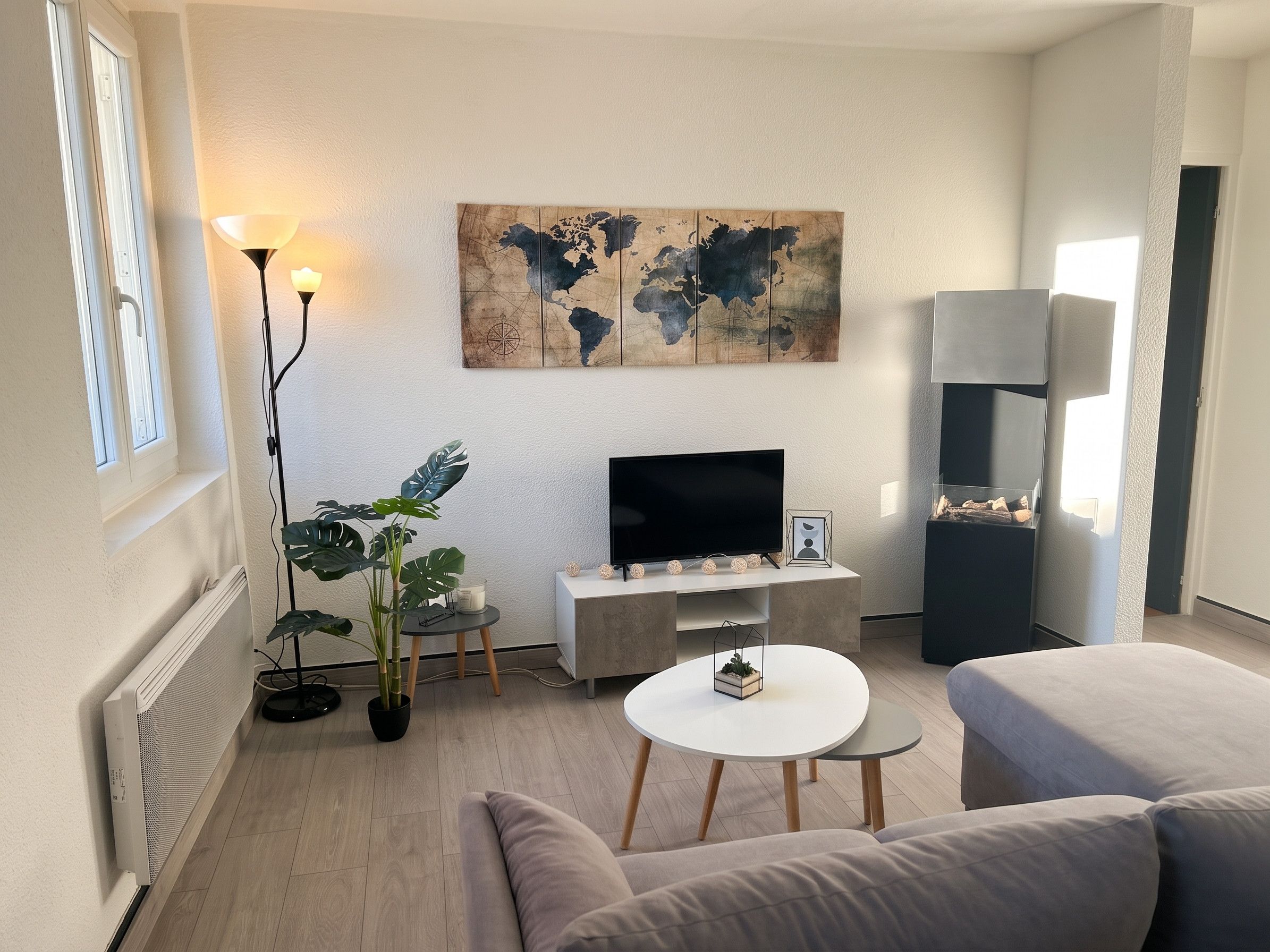 Ein modernes Wohnzimmer mit Fernseher, einer Weltkarte als Wandbild, einer Zimmerpflanze und einem Sofa.