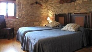 Ein Zimmer mit zwei Betten, Steinwänden, einer Holzbalkendecke und einem Fenster mit Vorhängen.