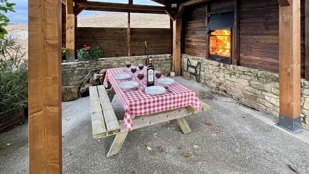 Eine Holzkreuzpergola mit einem karierten Esstisch, einer Steinmauer und einem Kamin.