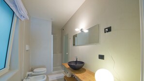 Ein Badezimmer mit Toilette, Waschbecken, Holz-Waschtisch, großem Spiegel und Duschbereich.
