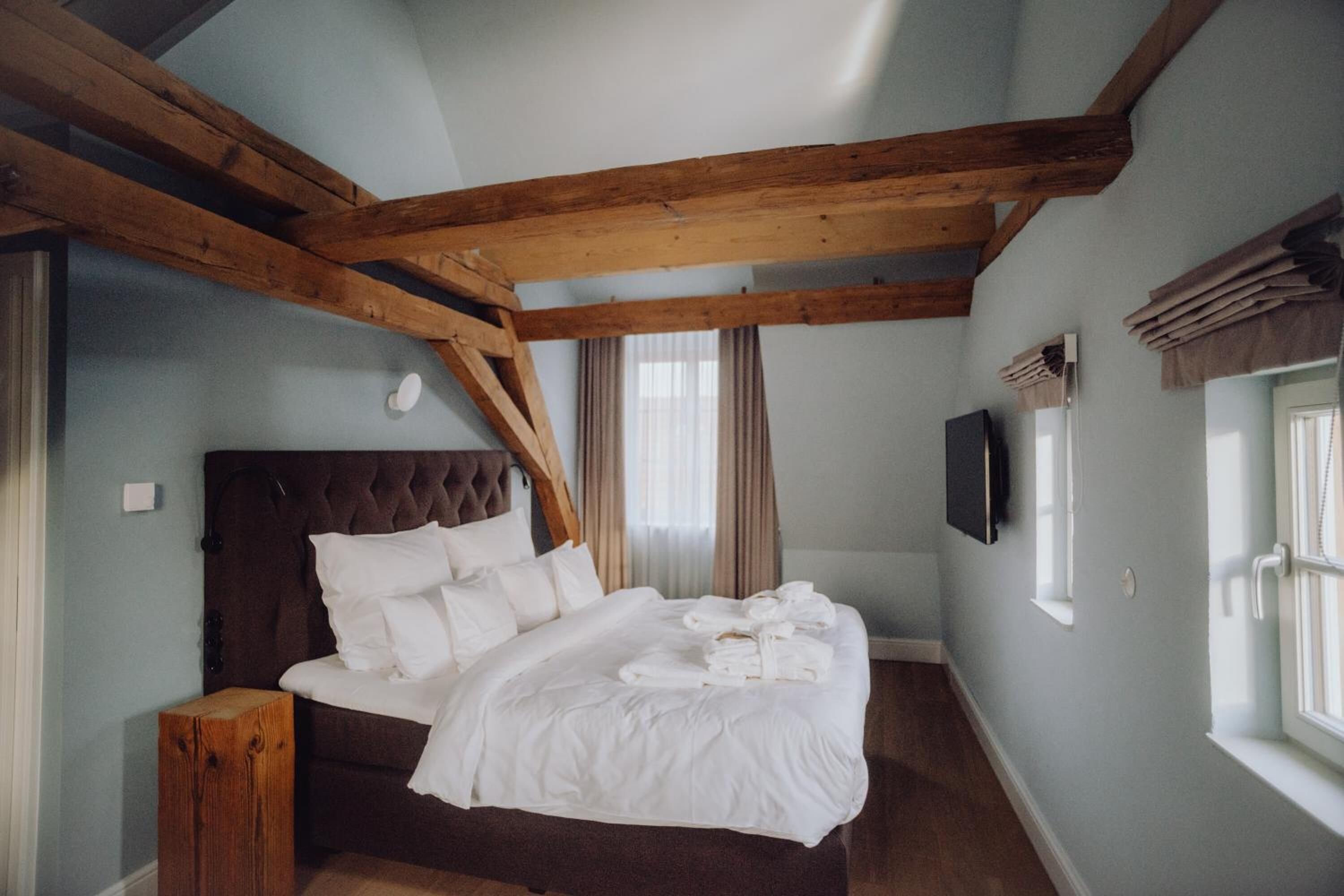 Ein Schlafzimmer mit einem großen Bett, Holzbalken, einem Fernseher und einem Fenster mit Vorhängen.