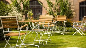 An outdoor seating area with wooden tables and chairs, surrounded by greenery and a stone building with arched windows. - GUT LEBEN am Morstein (Westhofen)