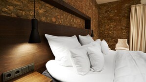 A neatly made bed with white bedding and multiple pillows, a wooden headboard, and a stone wall in the background. - GUT LEBEN am Morstein (Westhofen)