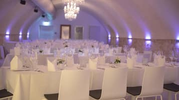 Un salón de banquetes con mesas y sillas blancas, una araña y un techo blanco.