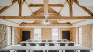 A conference room with a long table, wooden beams, stone walls, and large windows. - GUT LEBEN am Morstein (Westhofen)