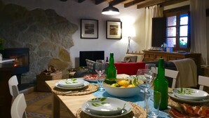 A dining area with a stone wall, wooden beams, a fireplace, and a table set for a meal. - "Casa Sira", a privilege for the senses (Villaviciosa)