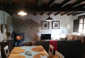 Un salon chaleureux avec un mur en pierre, une cheminée, un téléviseur et un coin repas agrémenté de sets de table.