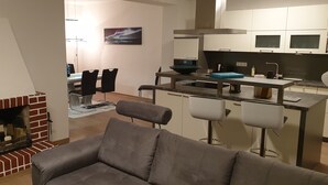 Ein modernes Wohnzimmer mit Kamin, einem Essbereich mit Stühlen und einer Küche mit Bar.