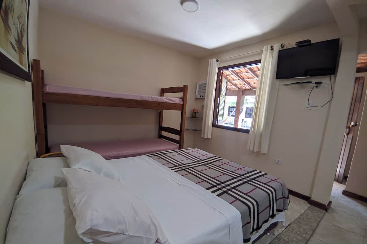 Ein Zimmer mit Etagenbetten, einem an der Wand befestigten Fernseher und einem Fenster mit Vorhängen.