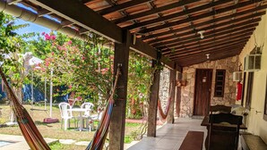A covered patio area with a hammock, outdoor seating, and a stone building in the background. - Pousada Roça Velha (Arraial do Cabo)