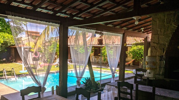 A poolside area with a covered seating area, a table, and chairs. - Pousada Roça Velha (Arraial do Cabo)