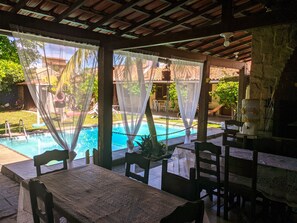 Zona junto a la piscina con un área de estar cubierta, una mesa y sillas.