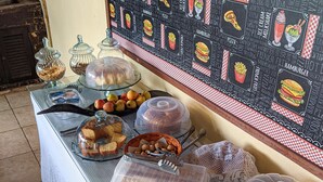 A buffet table with various food items covered in plastic, including bread, pastries, and fruits. - Pousada Roça Velha (Arraial do Cabo)