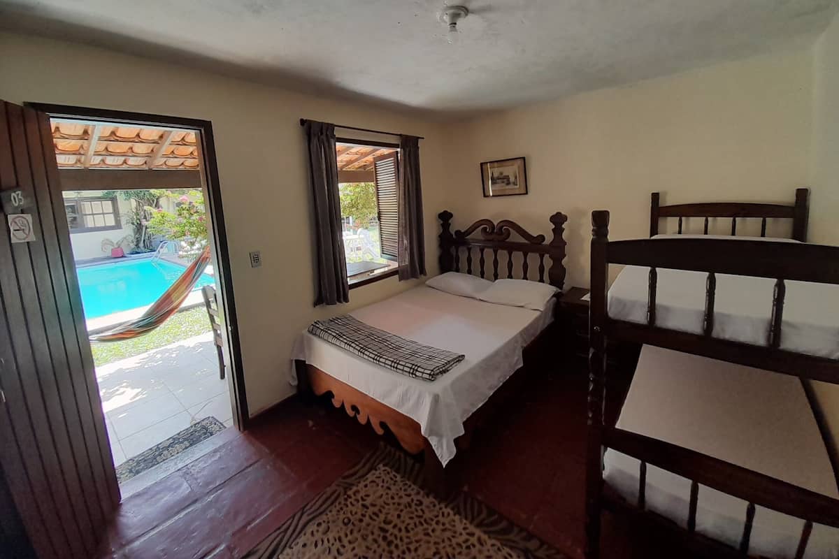 Ein Schlafzimmer mit einem Bett, einem Holzkopfende, einem Fenster mit Vorhängen, einer Tür, die zu einem Pool führt, und einem kleinen Teppich.