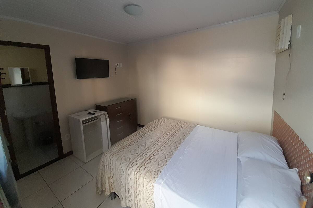 Ein Schlafzimmer mit Bett, Kleiderschrank, Schreibtisch und Fernseher an der Wand.