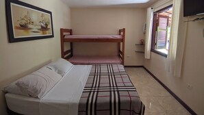 A small, compact room with a bunk bed, a single bed, a framed picture on the wall, a window with blinds, and a television mounted on the wall. - Pousada Roça Velha (Arraial do Cabo)