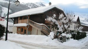 Een houten chalet met een houten trap naar een balkon, omringd door met sneeuw bedekte bergen.