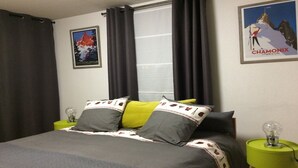 Een slaapkamer met een bed, twee bedlampen, een raam met gordijnen en twee posters aan de muur.