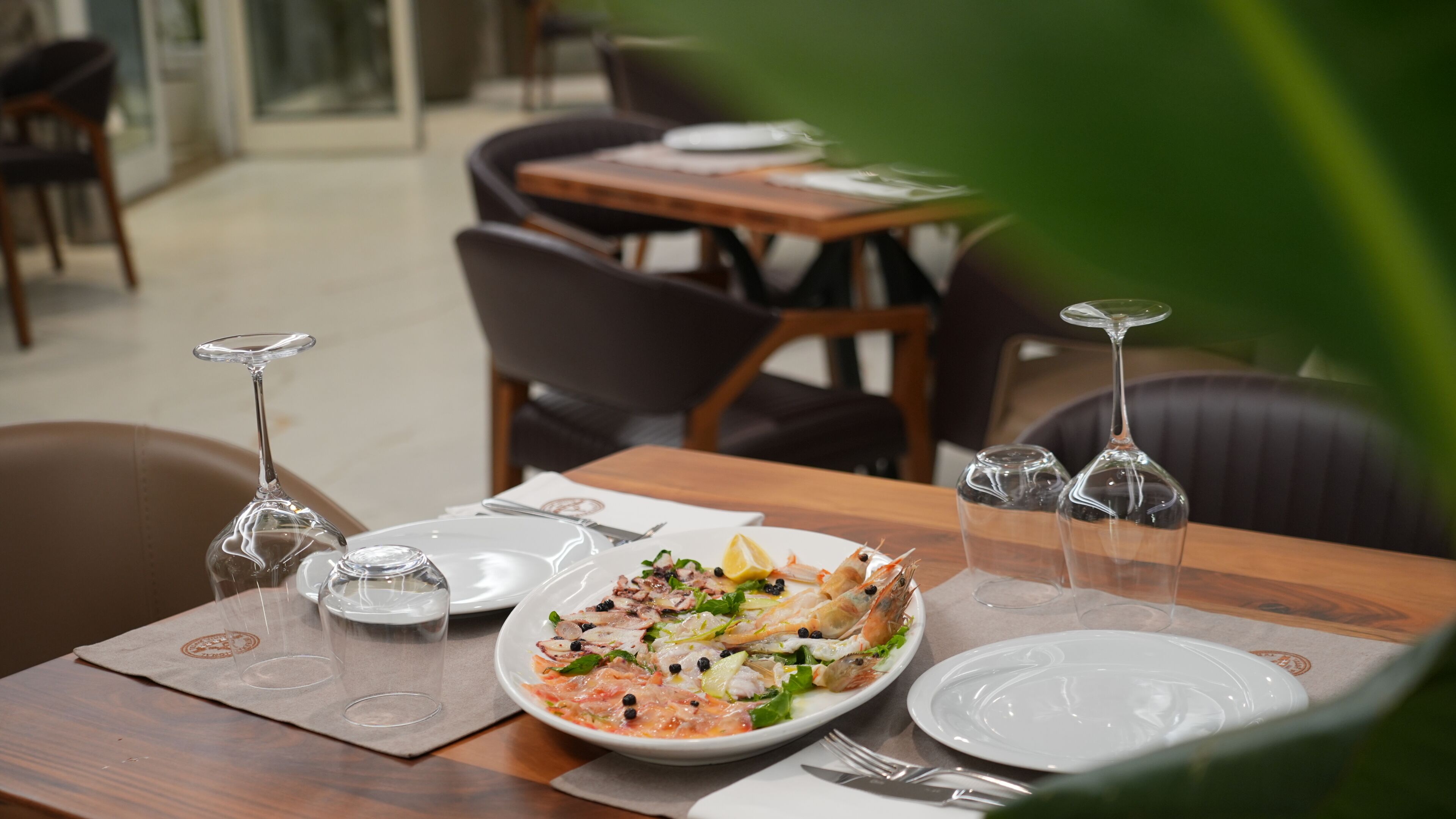 Une table à manger dressée avec des assiettes, des couverts et des verres à vin, et une assiette de nourriture placée au centre.