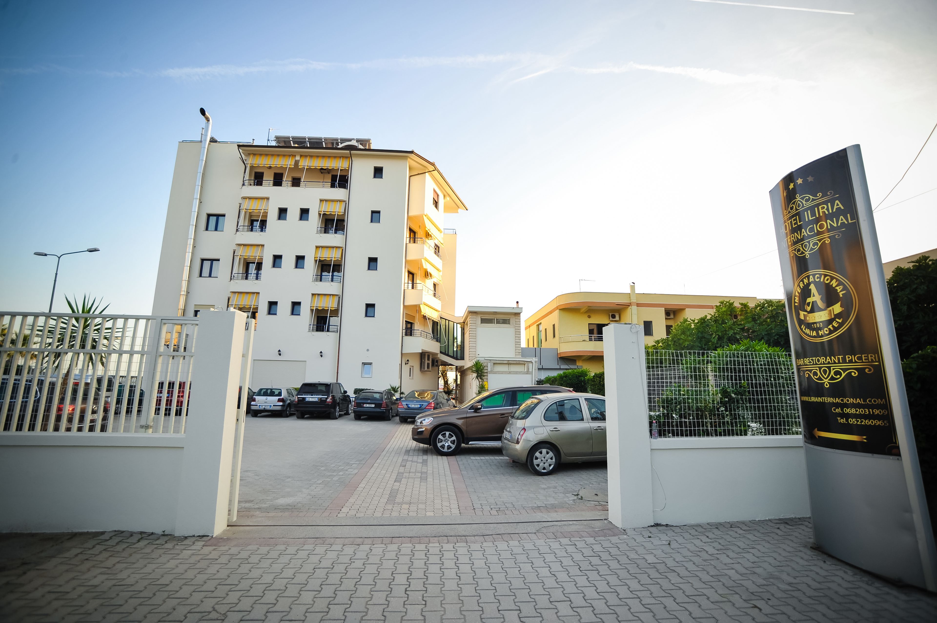A hotel entrance with a gated driveway, parked cars, and a signboard.