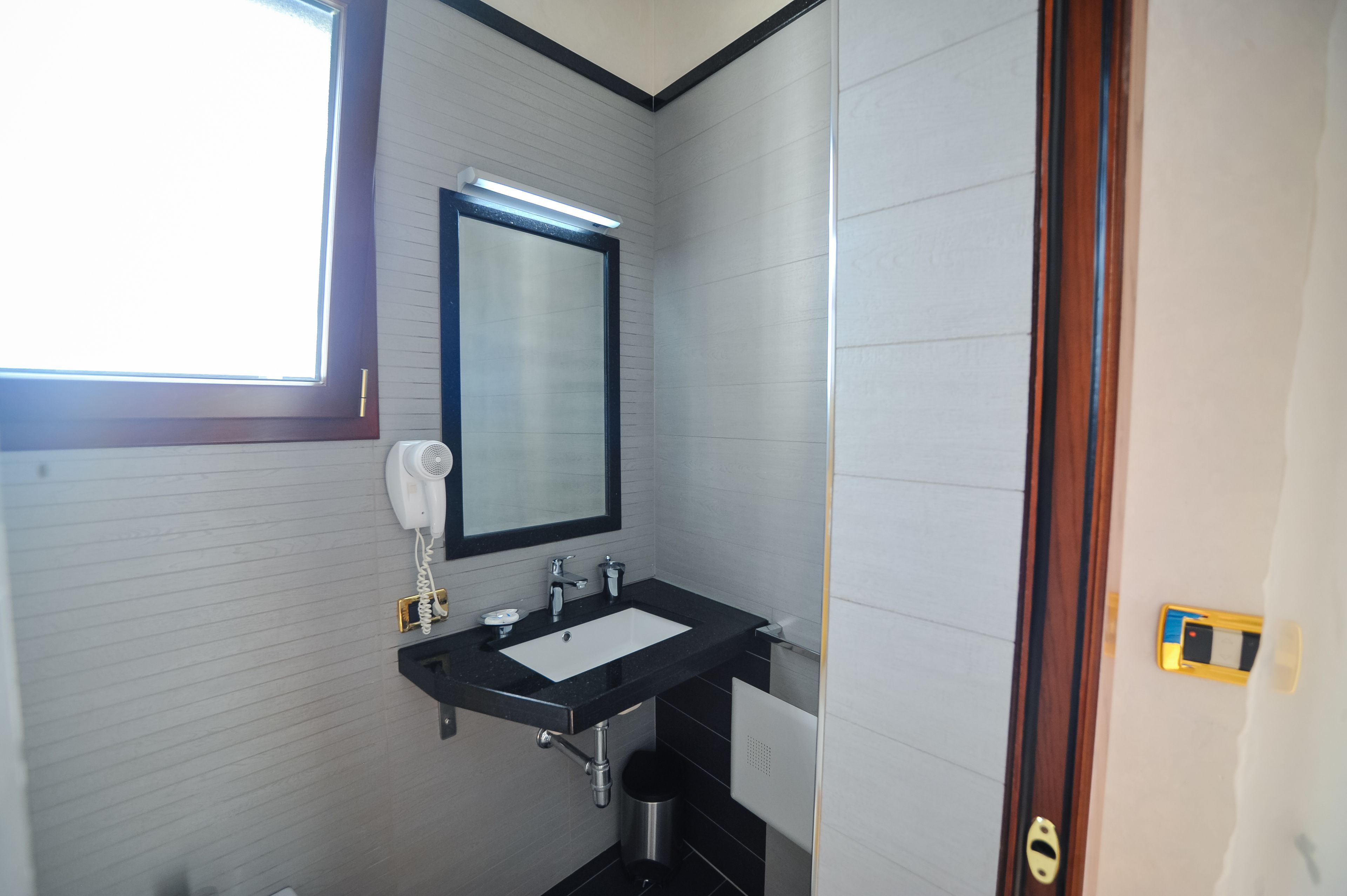 A bathroom with a black sink, white tiles, a mirror, and a window.