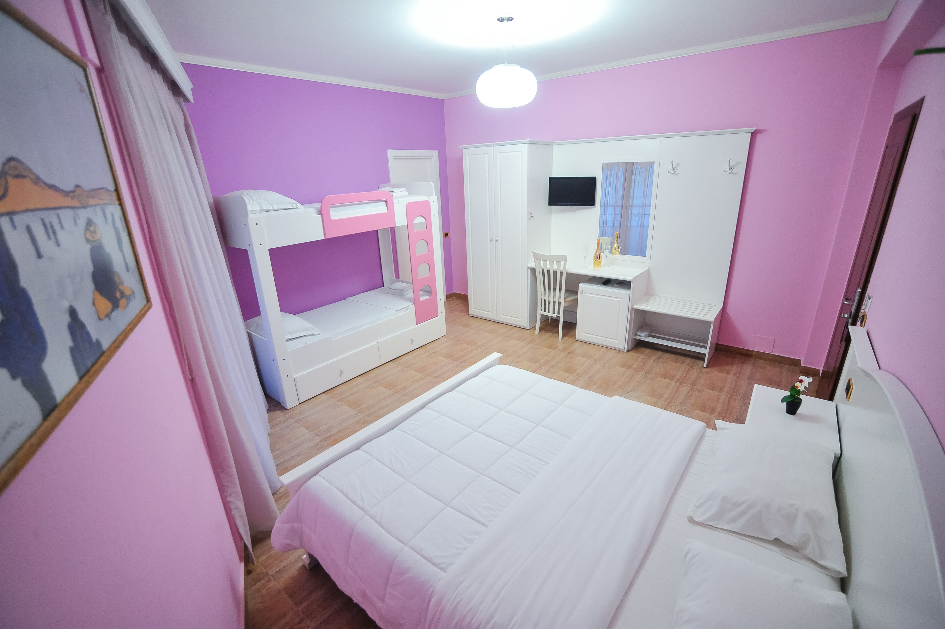 A room with a bunk bed, a desk with a chair, a wardrobe, and a bed.