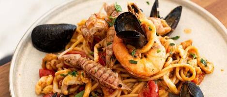 A plate of seafood pasta with mussels, shrimp, and squid, garnished with herbs.