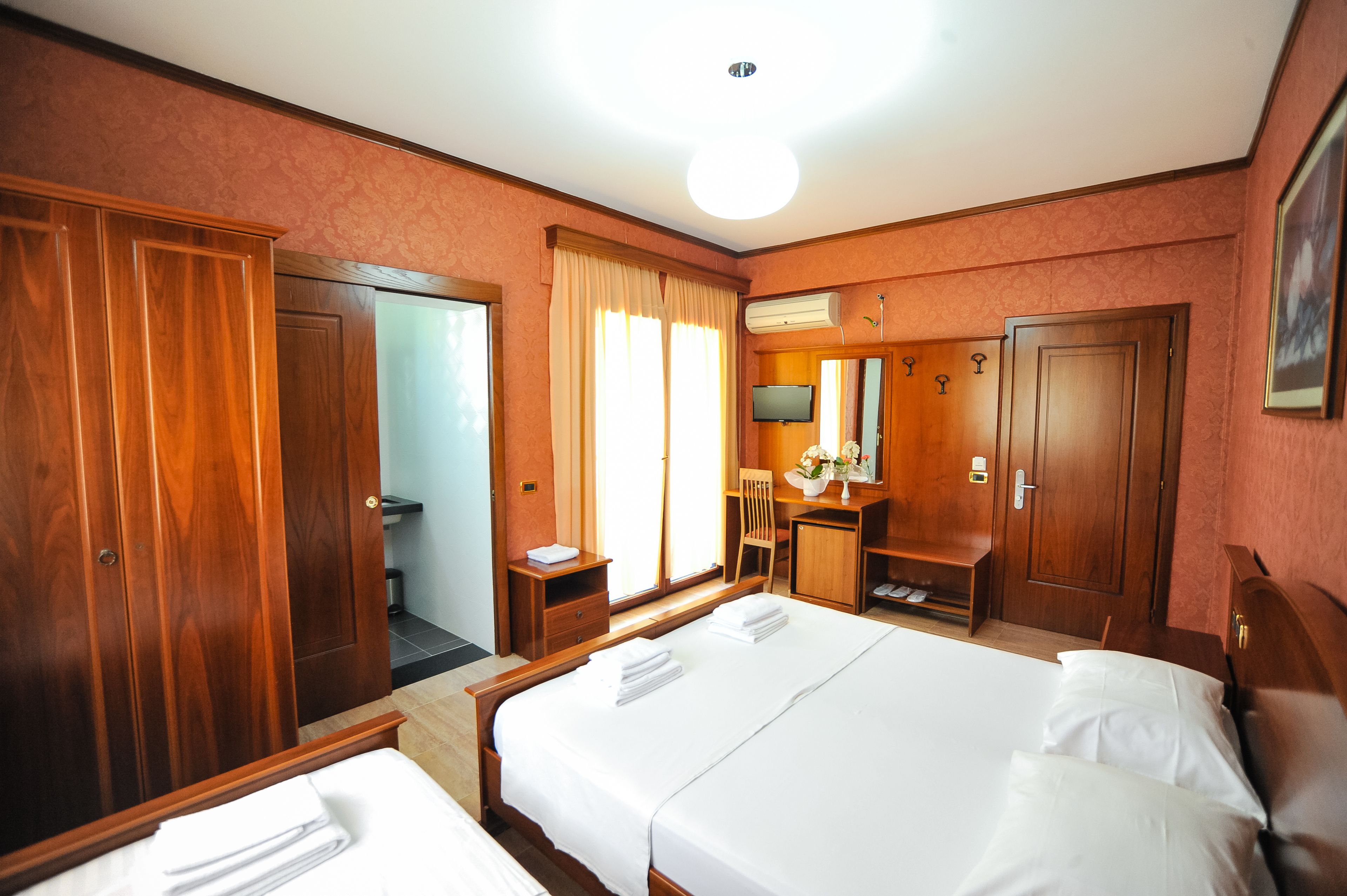Una camera d'albergo con due letti, una scrivania, una sedia, un armadio e un bagno.