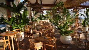 An outdoor patio with wooden tables and chairs, surrounded by potted plants and hanging wicker lamps. - Hotel Iliria Internacional (Durrës)